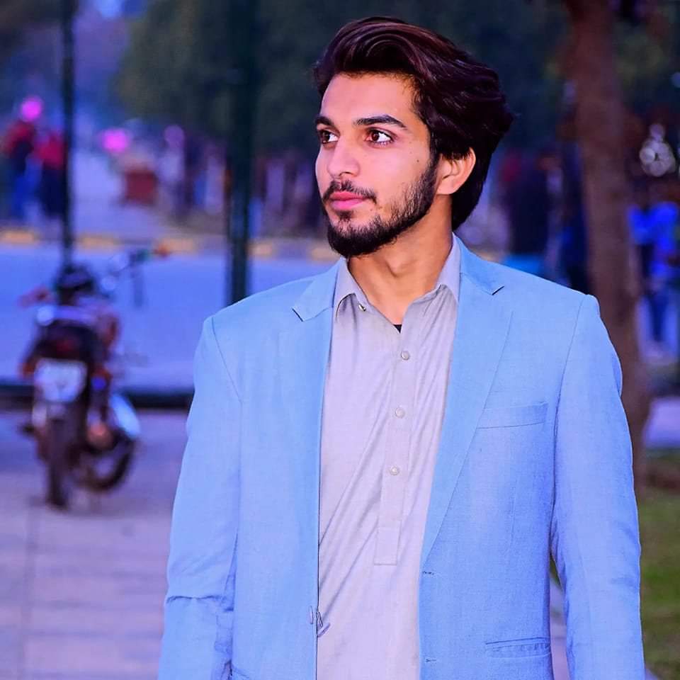 Portrait of Shahzaib Rehman Khattak, a man with short dark hair and a beard, wearing a black shirt, looking directly at the camera with a slight smile, against a dark background